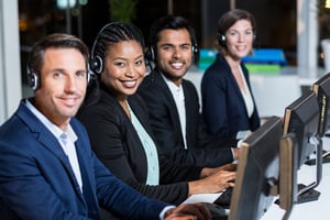 Portrait of group of business colleagues with headsets using computer at office desk