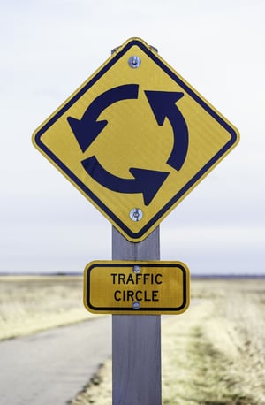 Traffic circle sign posted by pavement (shallow depth of field)